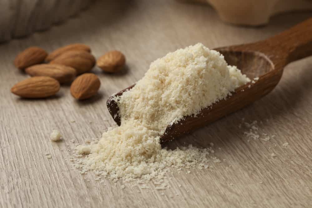Wooden spoon with almond meal and almonds