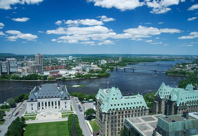 Aerial view of Ottawa and across the Ottawa River to Gatineau Quebec. Supreme court of Canada and gothic ministry buildings in foreground. Deep blue sky and clouds.