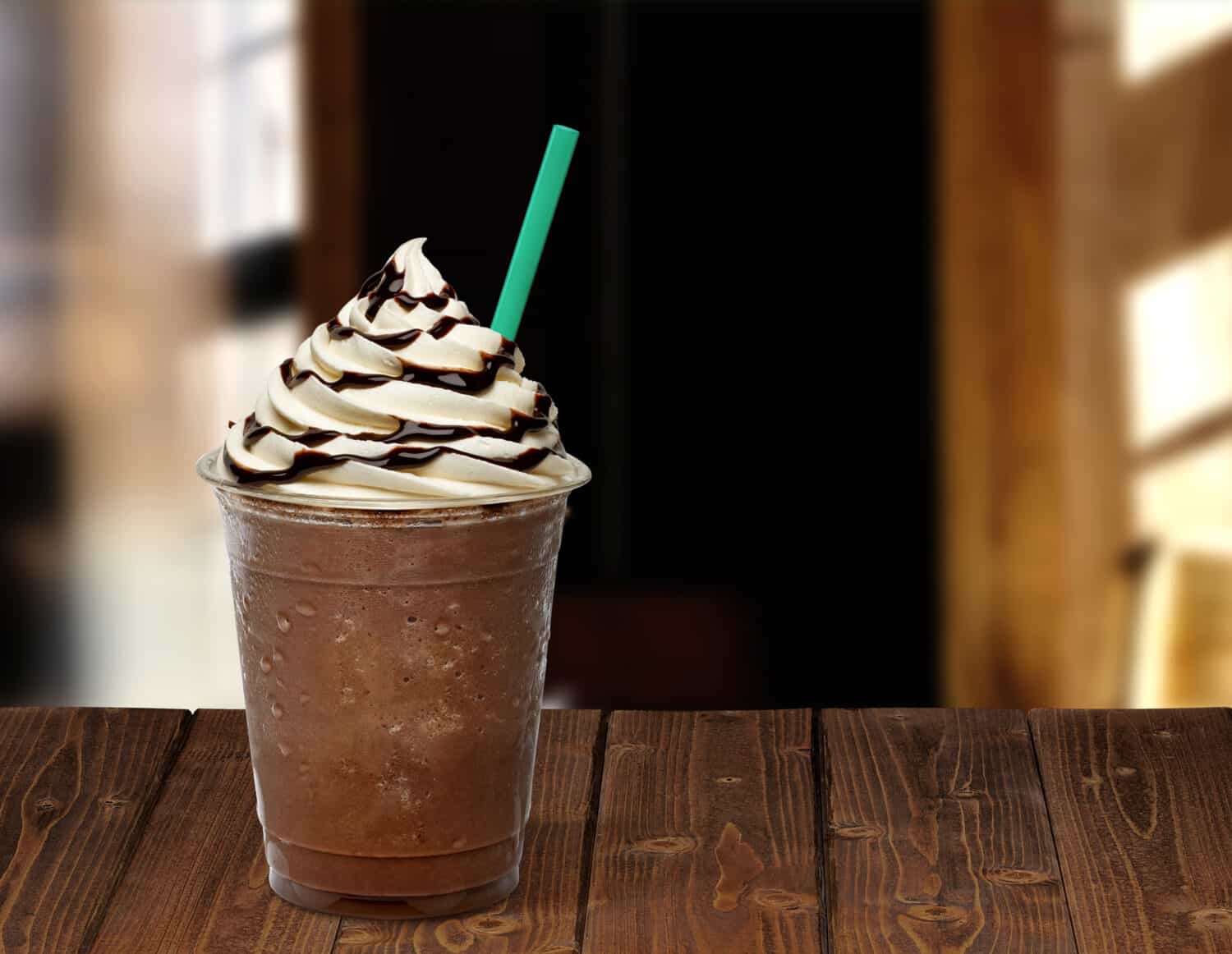 Frappuccino in plastic takeaway or to go cup on wooden table at cafe