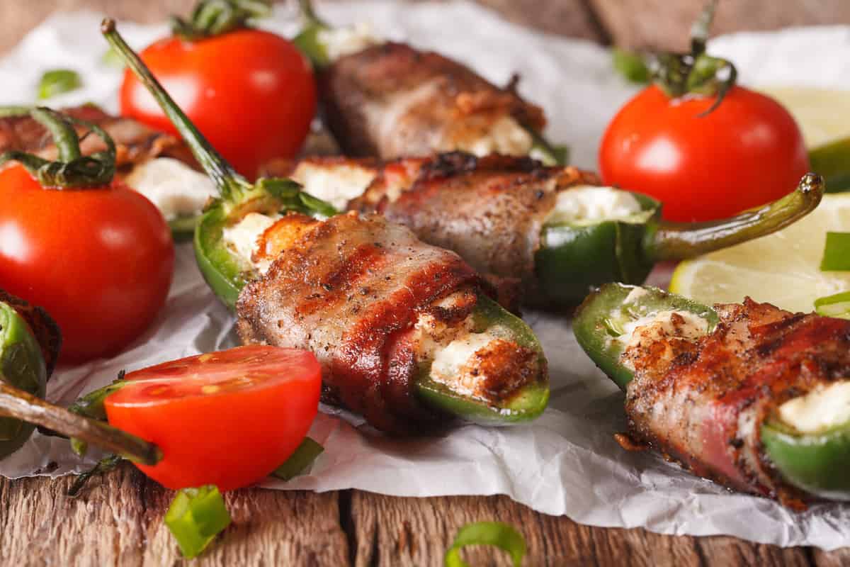 Spicy appetizer: jalapeno peppers stuffed with cheese wrapped in bacon close-up on the table. horizontal