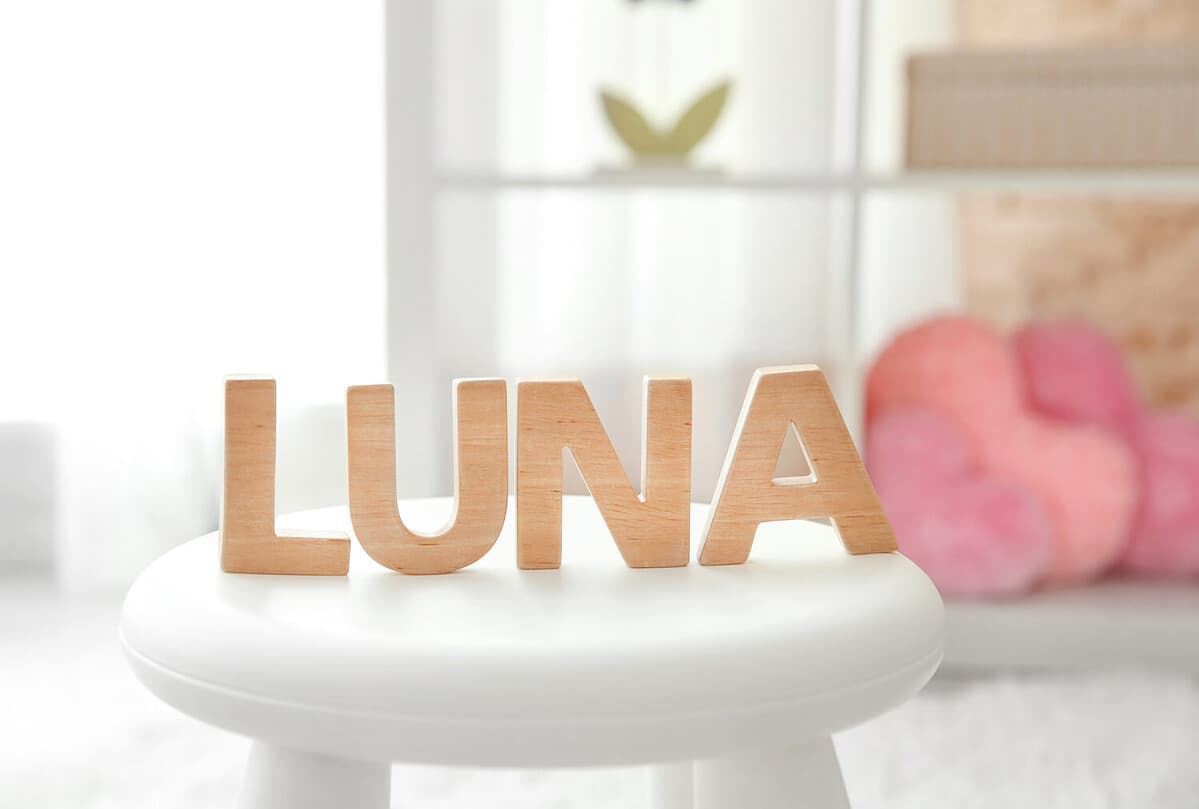Baby name LUNA composed of wooden letters on stool. Choosing name concept