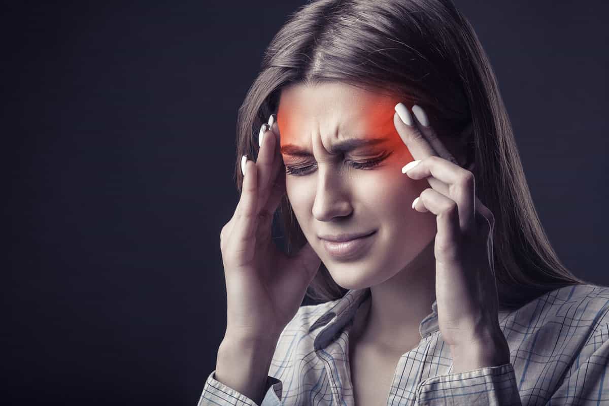 Young woman is suffering from a headache against a dark background. Studio shot