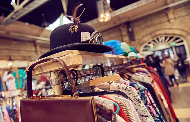 Vintage second hand hat and clothes rail showing colourful vintage clothes on coat hangers.