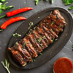 Grilled spare ribs on plate over black stone background. Tasty bbq meat. Top view, flat lay