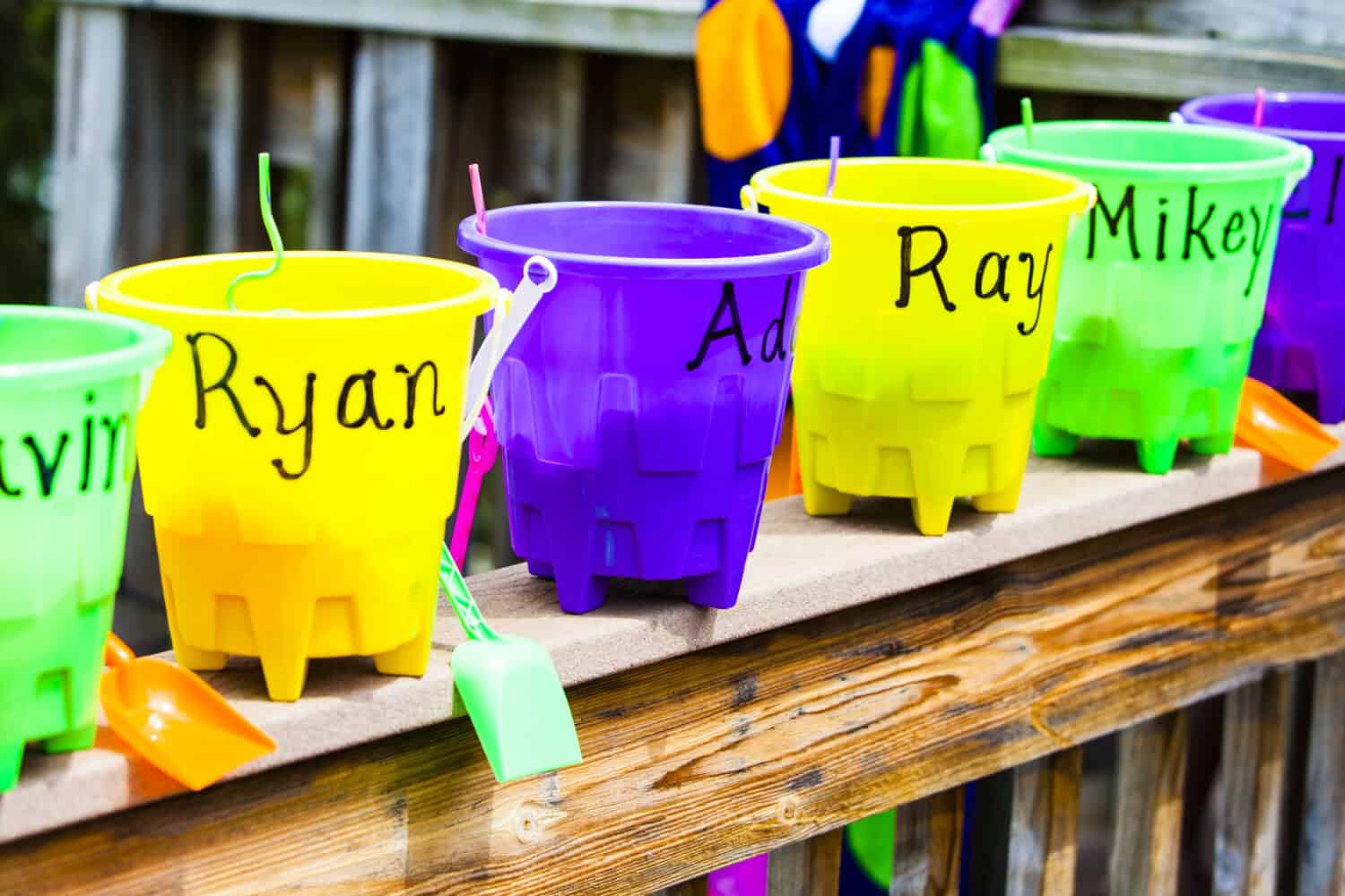 Beach party favors. Buckets with each child's name filled with candy and toys, lined up outside on a wooden rail