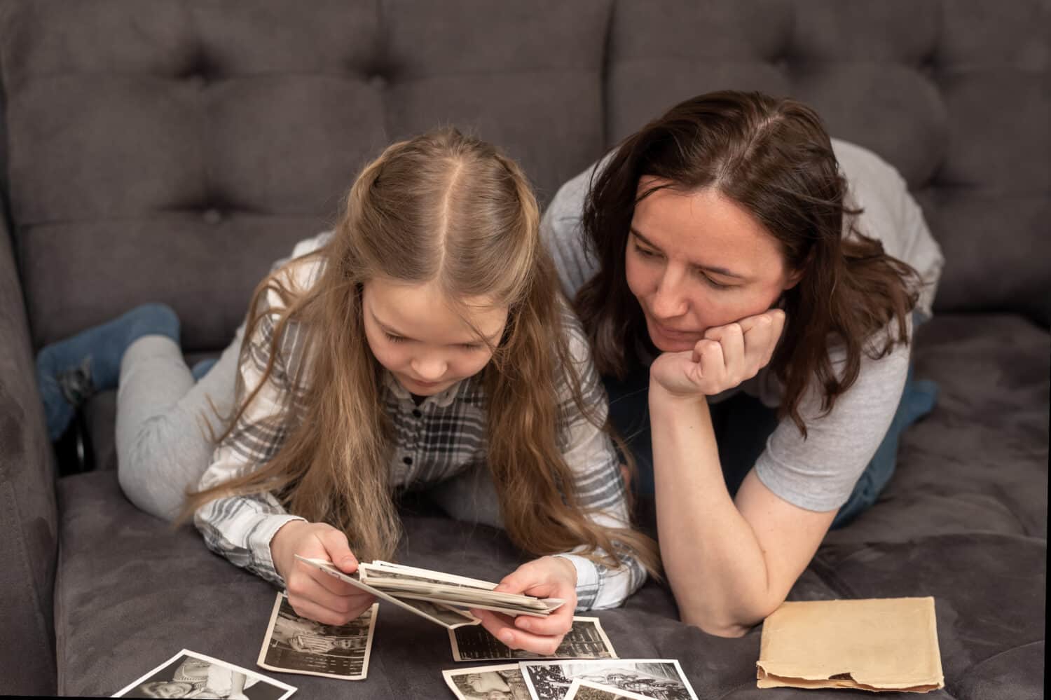 mom and daughter are lying on the couch and looking at the family photo archive. Family, trust, succession concept.