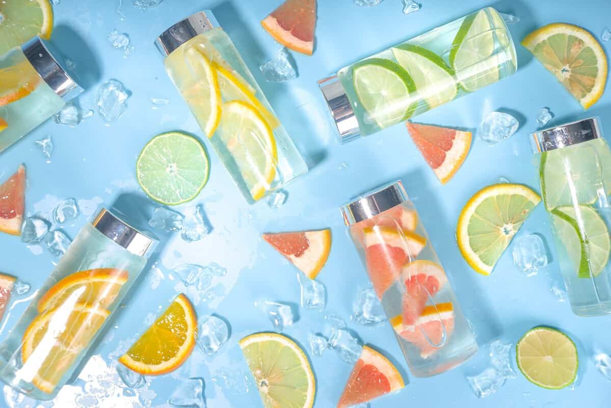Variety of cold drinks in bottles, summer infused water bottles, lemonade healthy cocktails with different citrus fruits - lemon, orange, grapefruit, lime, bright background copy space