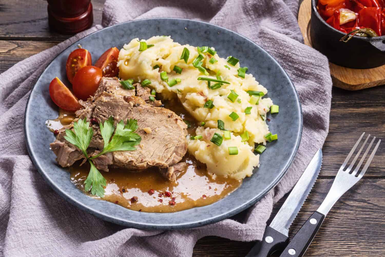 Baked pork with mashed potatoes and green scallion on plate, close-up