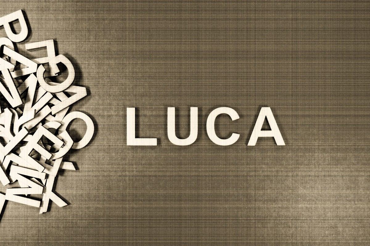 Popular and modern baby boy fashion name LUCA in wooden English language capital letters spilling from a pile of letters on a green background in sepia