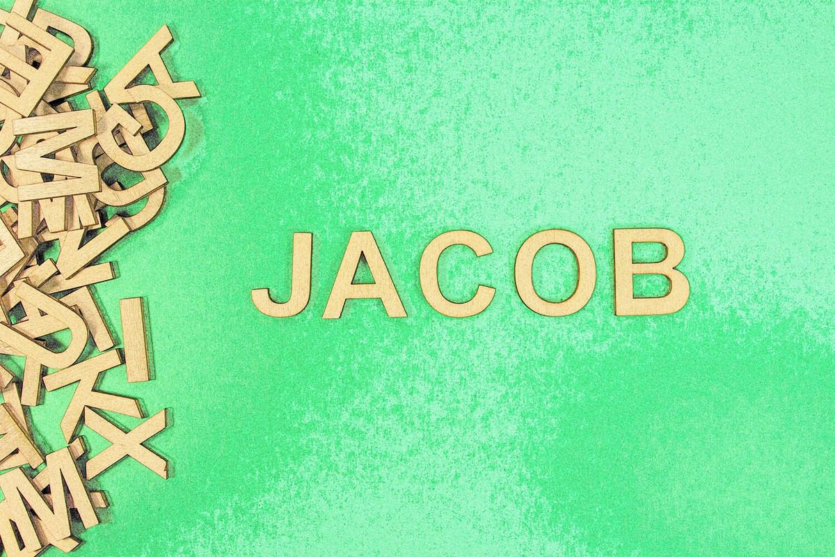 Popular and modern baby boy fashion name JACOB in wooden English language capital letters spilling from a pile of letters on a green background pencil sketch