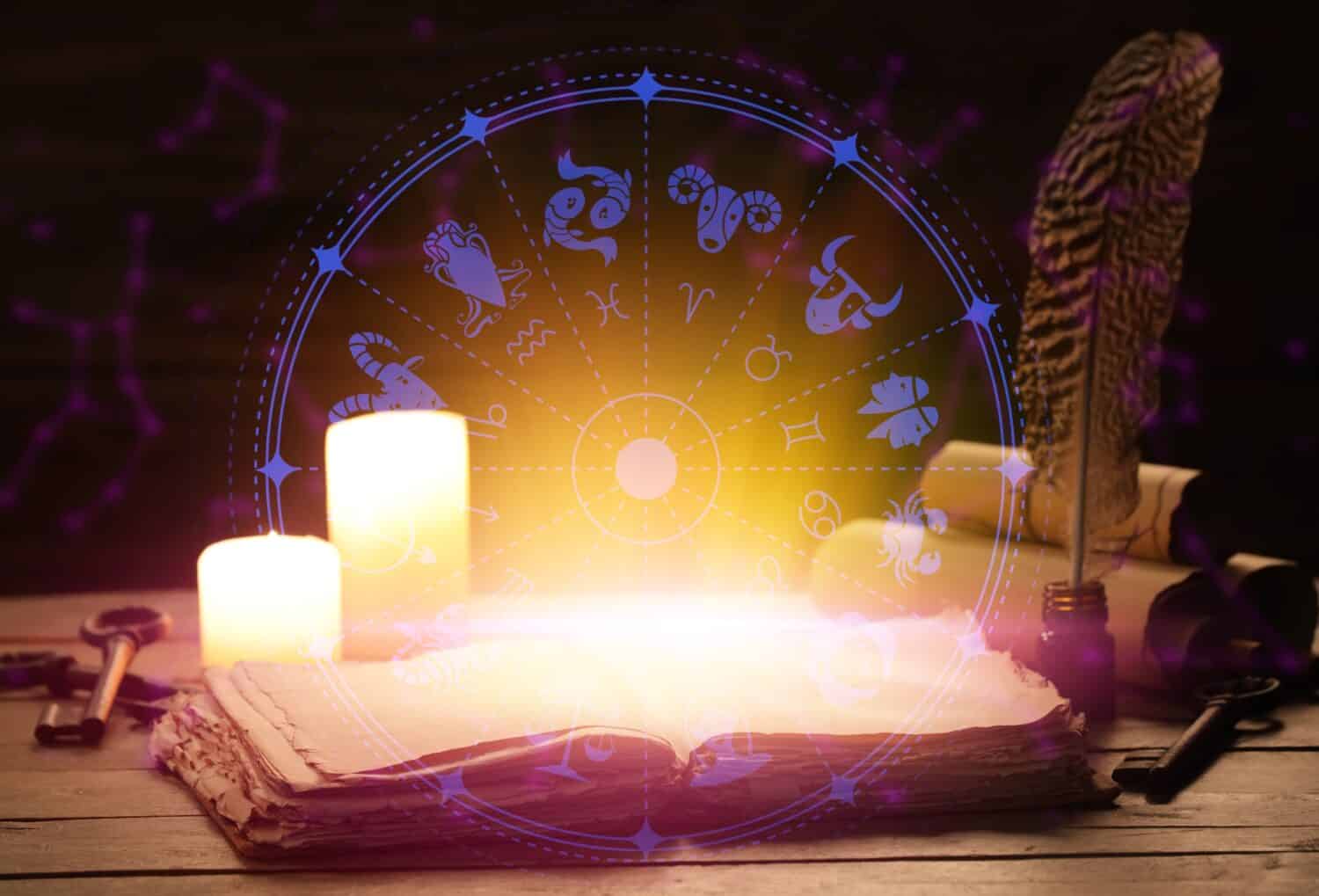 Open book, candles and astrological signs on table against dark background