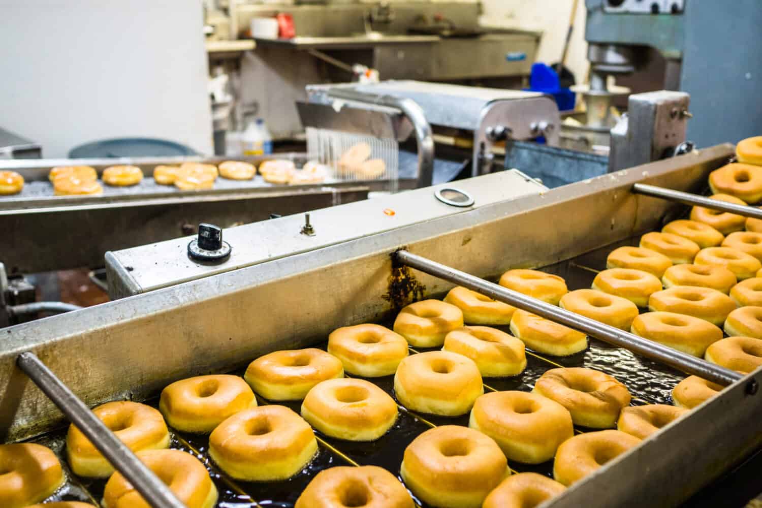 Donuts are fried, glazed, and put on racks in a doughnut shop bakery. 