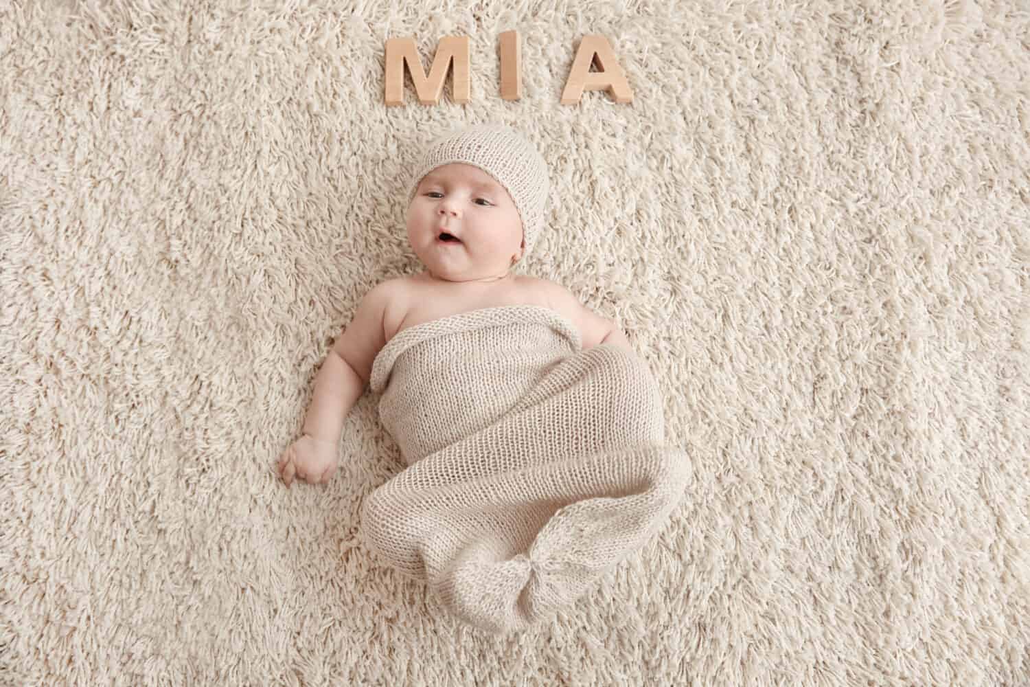 Cute baby with word MIA lying on carpet. Choosing name concept