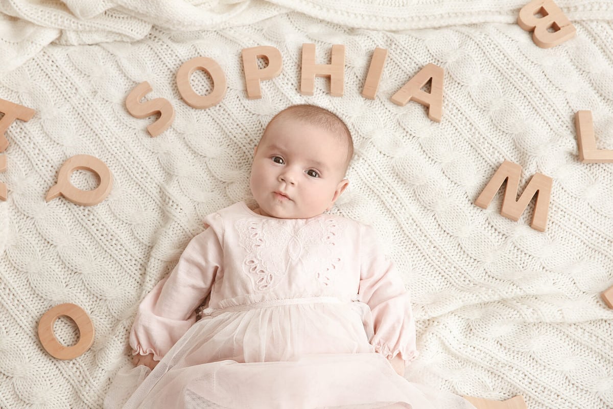 Cute baby with word SOPHIA lying on soft blanket. Choosing name concept
