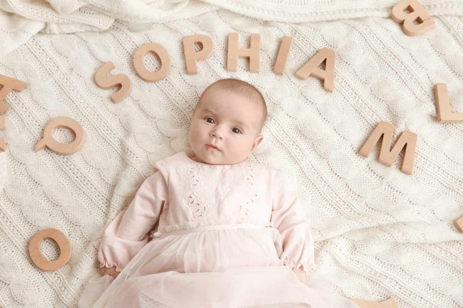 Cute baby with word SOPHIA lying on soft blanket. Choosing name concept