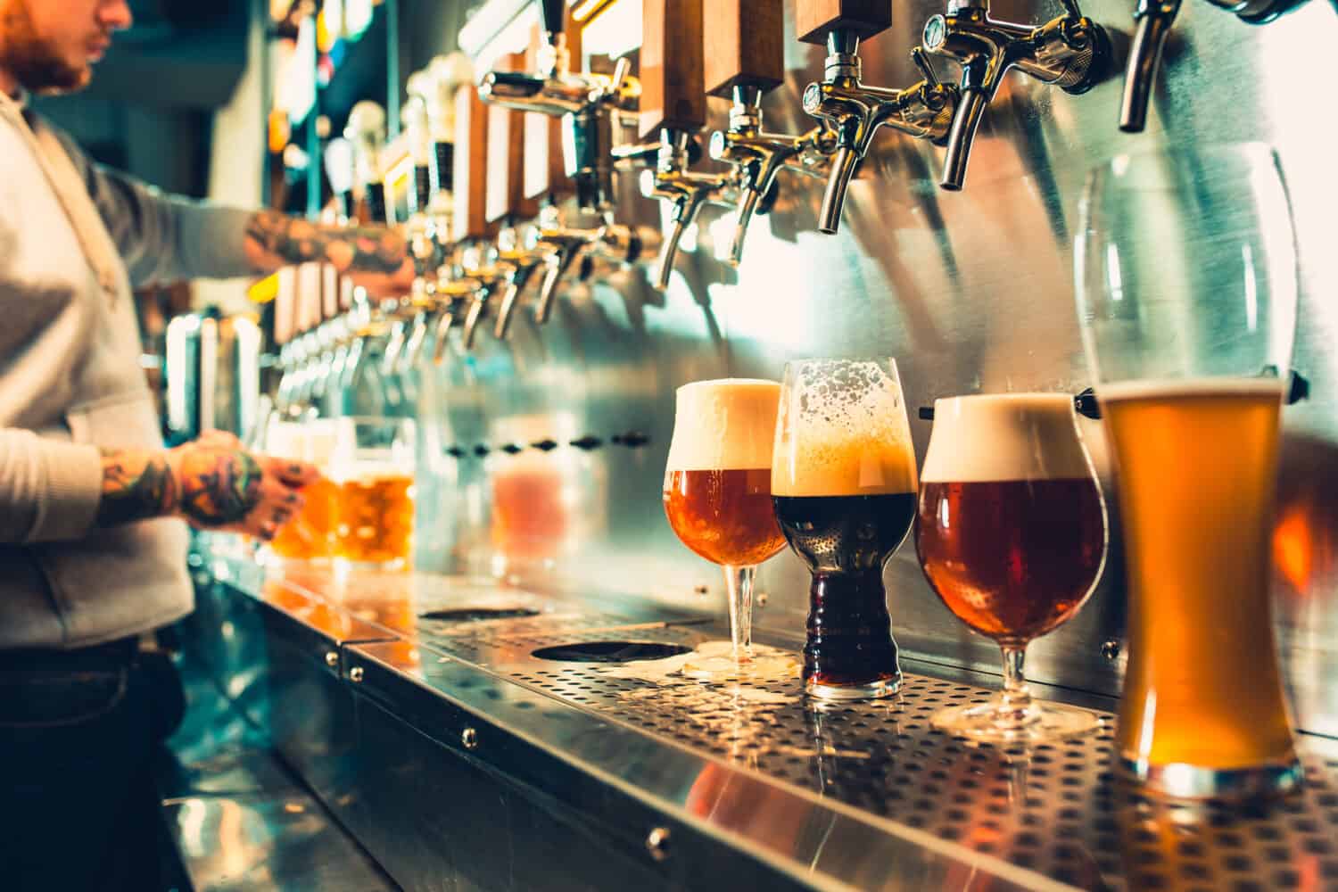 We meet oktoberfest. Hand of bartender pouring a large lager beer in tap. Pouring beer for client. Side view of young bartender pouring beer while standing at the bar counter