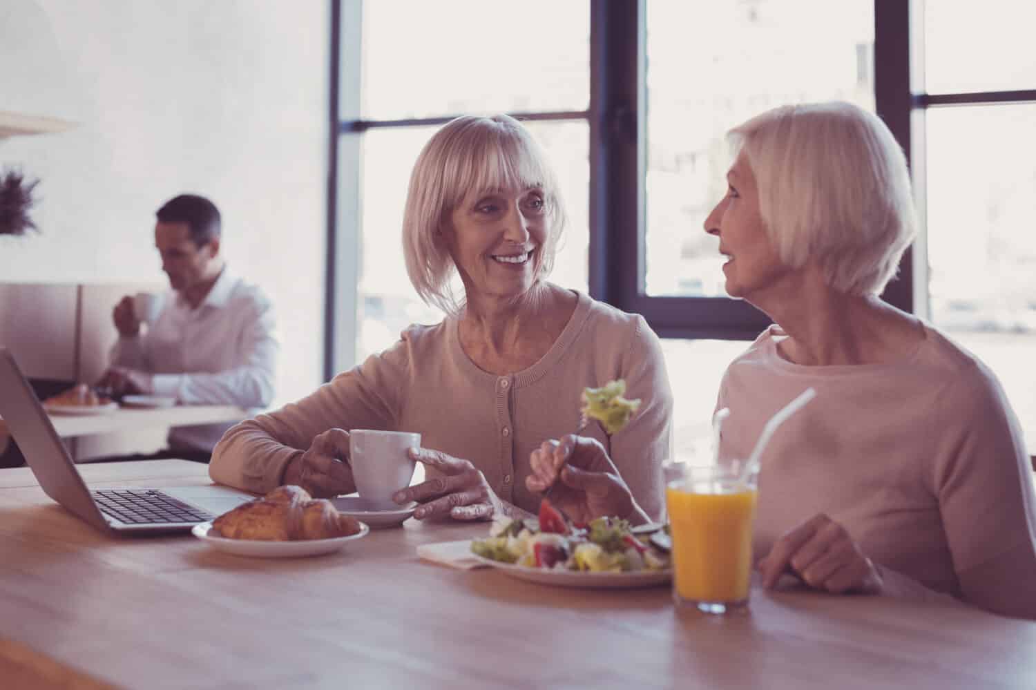 Lunch and talks. Interested attentive senior woman sitting in the restaurant drinking tea and listening to her girlfriend.