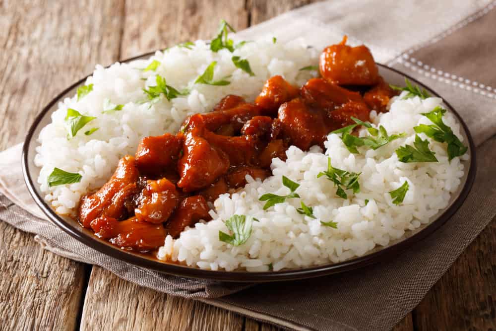 Menu in rustic style: Bourbon chicken in a sauce with whiskey, served with rice on a plate on the table. horizontal