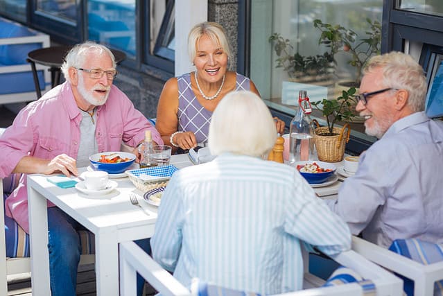Pleasant meeting. Happy aged people talking during the meal while relaxing together in the restaurant