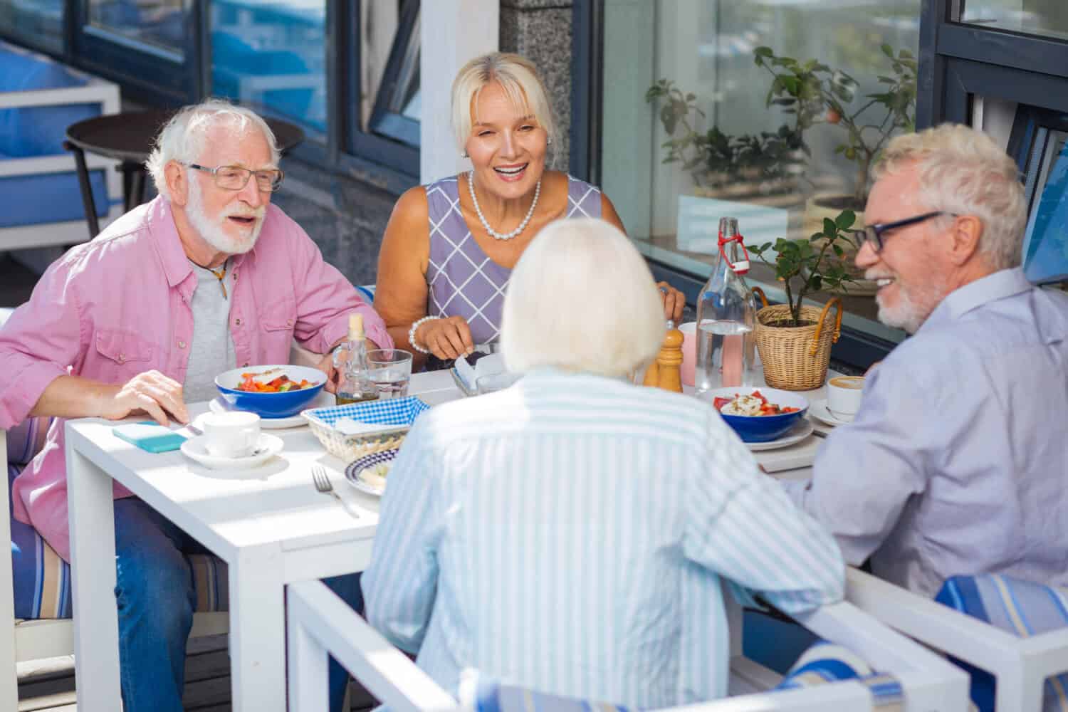 Pleasant meeting. Happy aged people talking during the meal while relaxing together in the restaurant