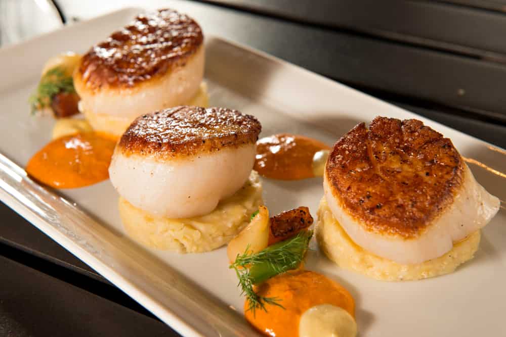 Pan Seared Diver Scallops with Polenta on a white serving dish