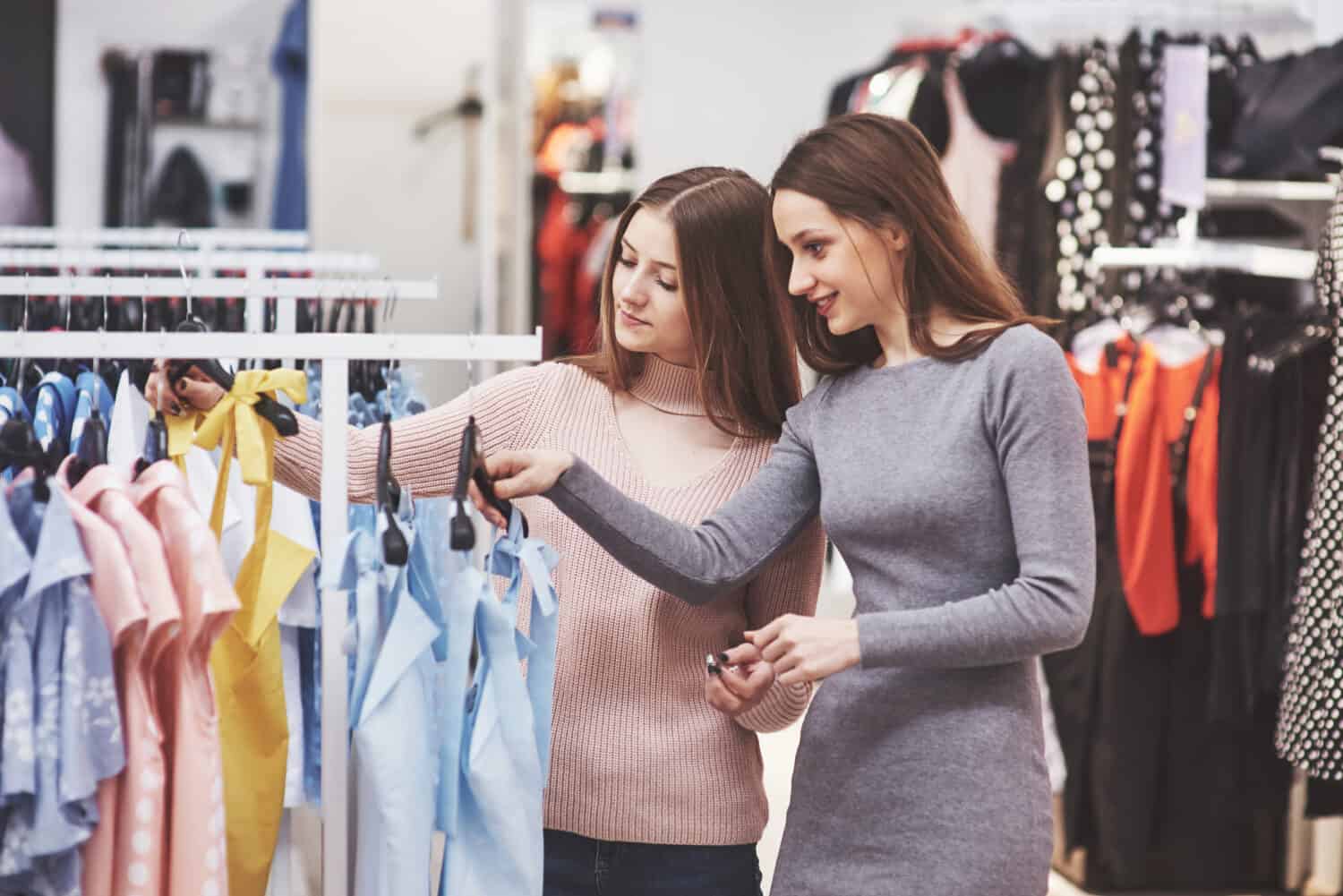 The best friends together spend time. Two beautiful girls make purchases in the clothing store. They dressed in the same clothes.