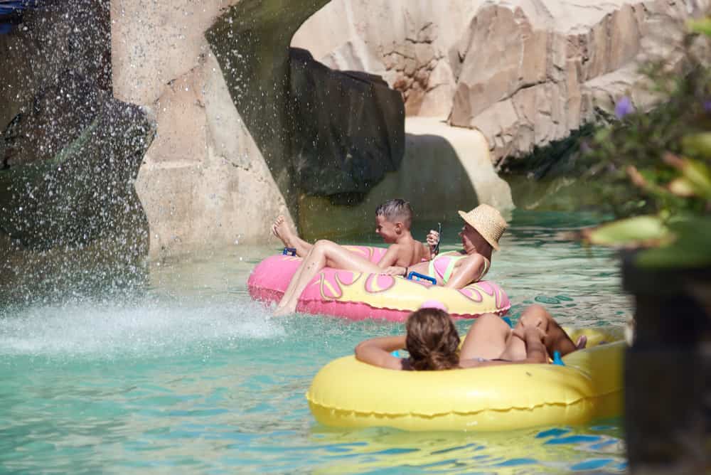 Cute European boy and his mother are spending amazing time at Waterland. They are swimming along the lazy river and fake waterfall. A lot of drops are everywhere. They are on the holidays.