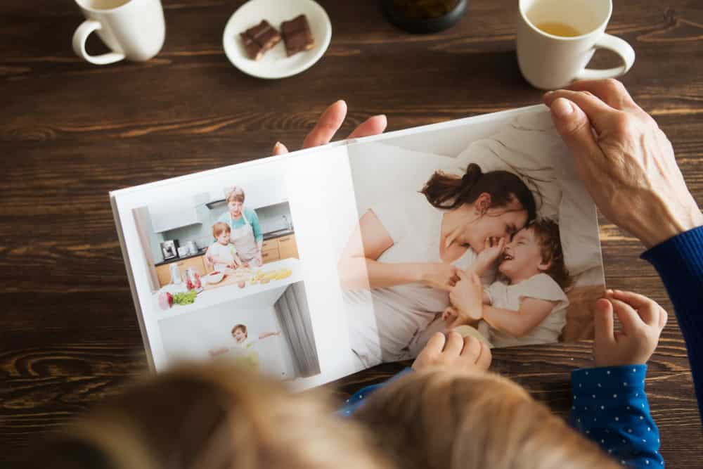 Hand senior woman and child holding a family photo album against the background of the a wooden table.