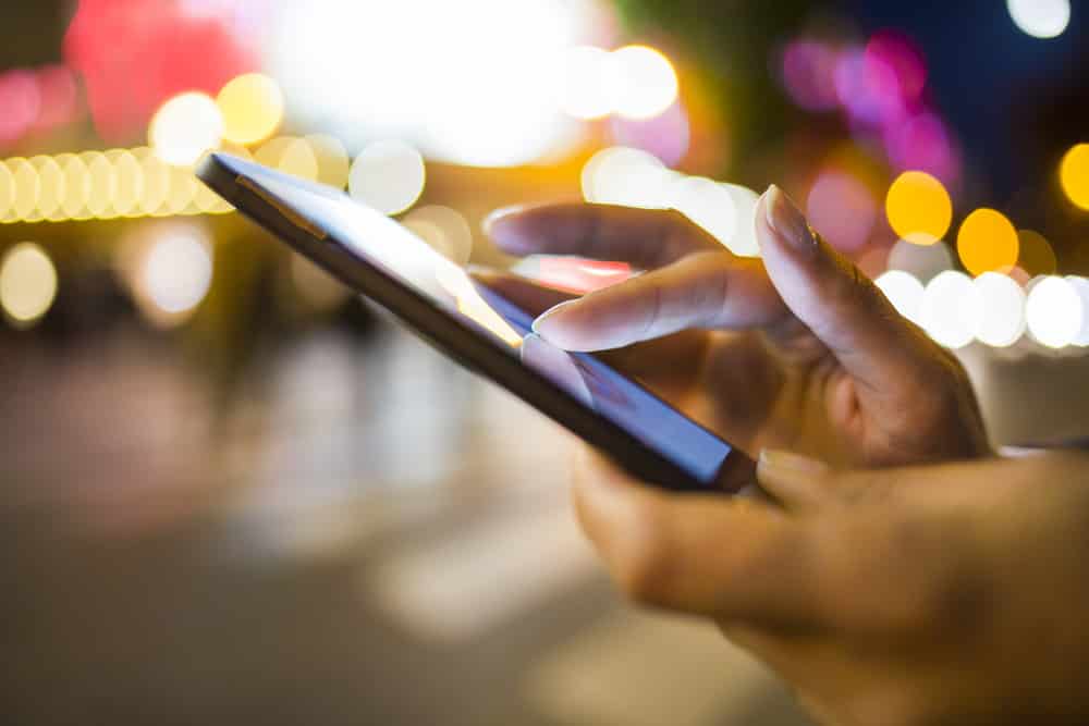 Woman using her Mobile Phone in the street, night light Background