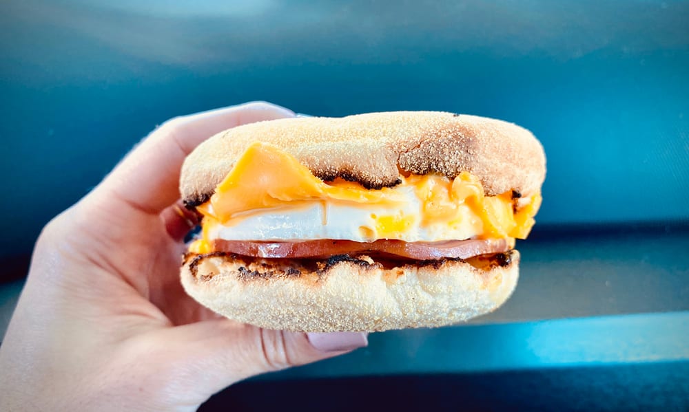 Person Holding Breakfast Sandwich with Egg Ham Bacon and Cheese on Toasted English Muffin
