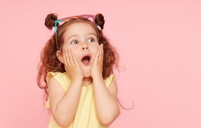 Portrait of surprised cute little toddler girl in sunglasses over pink background. Child model have fun and jump. Advertising childrens products