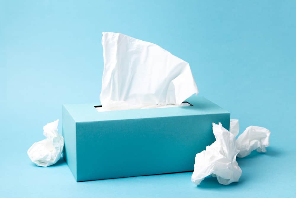 Light blue tissue box and crumpled tissues on blue background. Cold and flu concept. Minimal monochromatic composition.