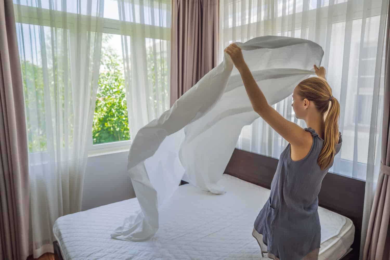 Young Female Housekeeper Changing Bedding In Hotel Room
