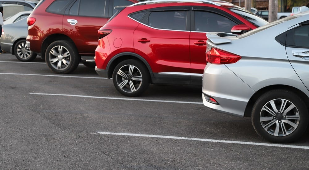 Closeup of rear, back side of blue car with other cars parking in outdoor parking area in bright sunny day.