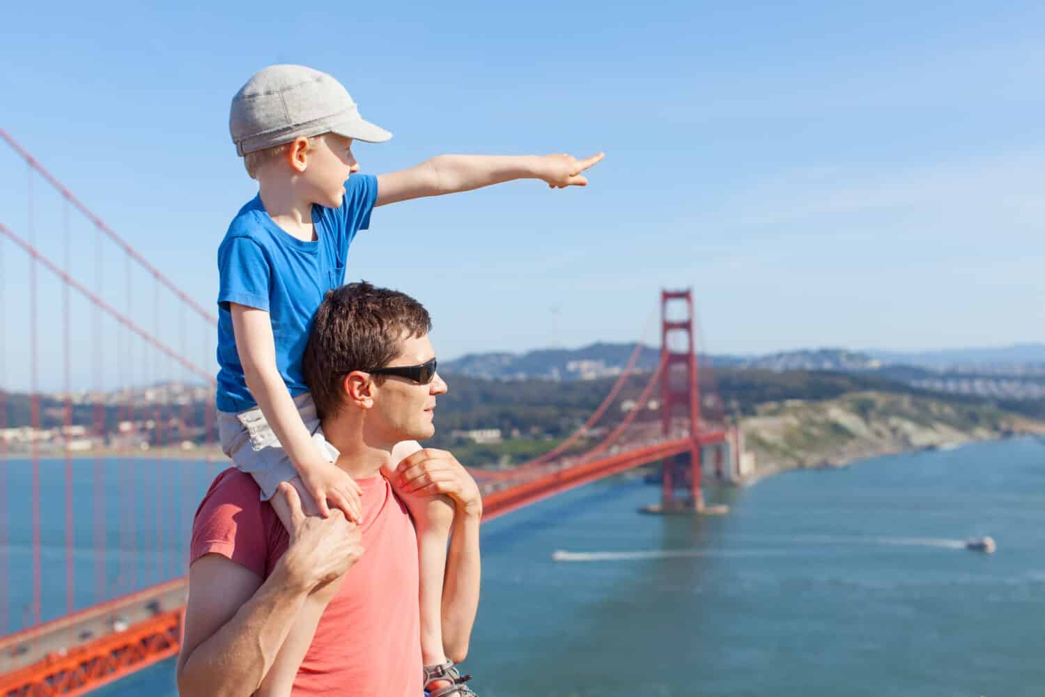 little son sitting at his father shoulders and enjoying together the view of golden gate bridge in san francisco, california