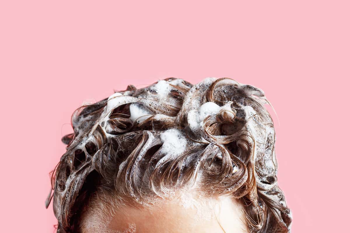 Fmale hair shampoo and foam on pink background close-up.