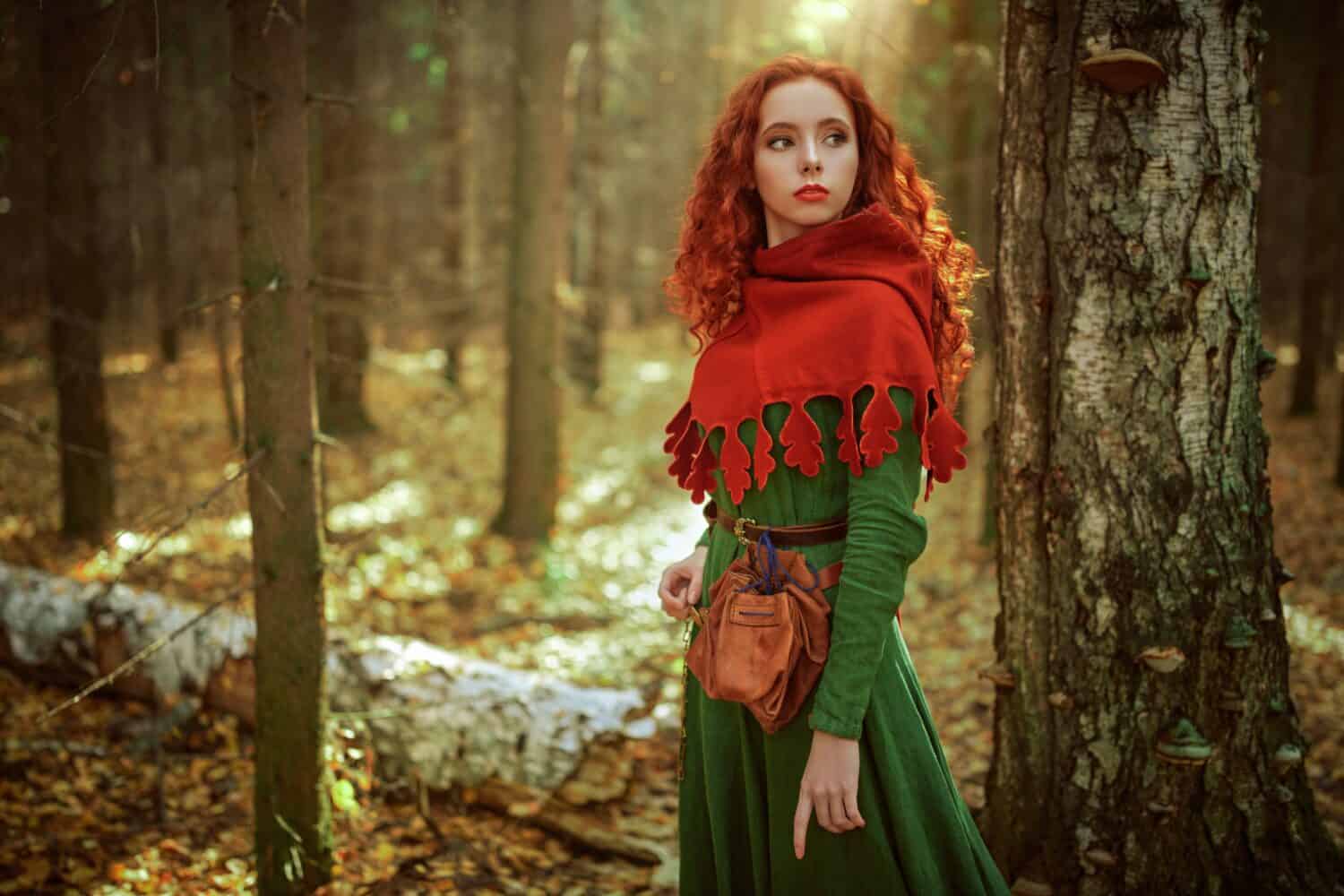 Celtic culture. Fantasy world. Portrait of a beautiful red-haired girl of the Middle Ages standing in the dense forest.