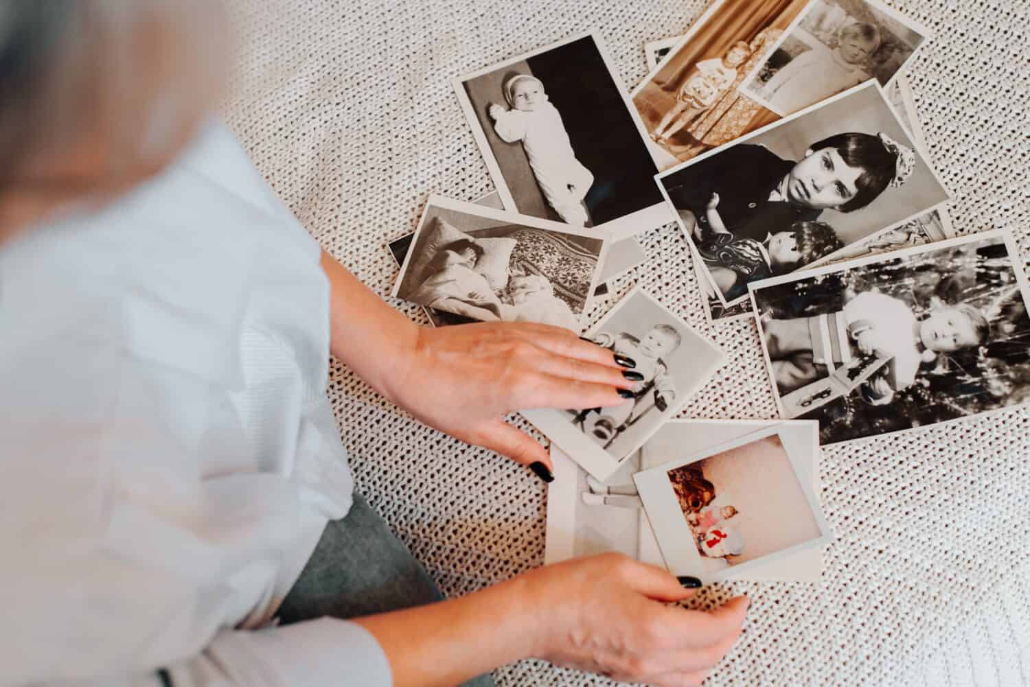 Memories of childhood, nostalgia of youth concept. Close-up of caucasian woman looking at her baby vintage photo while sitting on sofa, indoors. Selective focus on monochrome retro pictures, top view