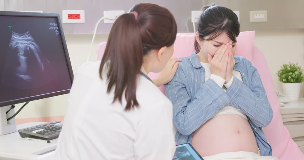 Pregnant woman feels sad when getting some bad news that her baby gets sick or intrauterine fetal demise - female doctor consoles her