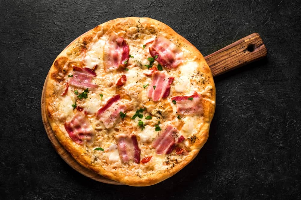 Bacon Pizza. Italian Carbonara Pizza with bacon and mozzarella cheese on black table, top view, close up.