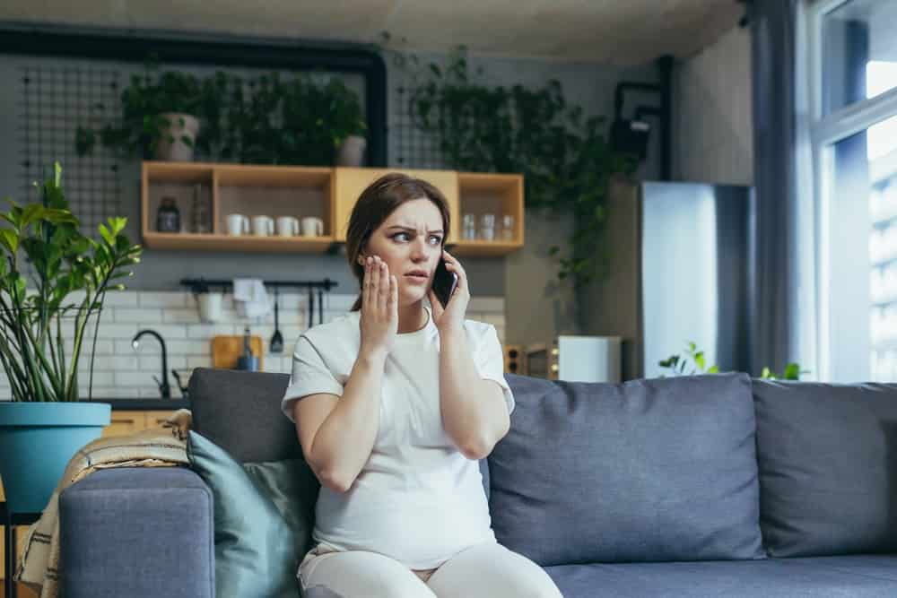 Sad pregnant woman at home anxious talking on the phone sitting on the couch
