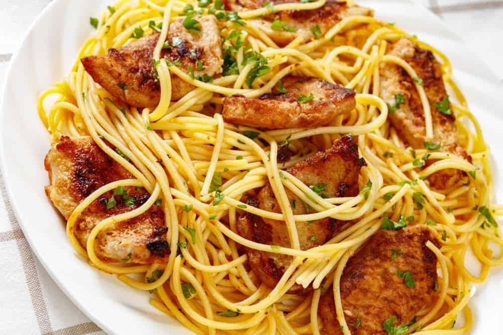 close-up of Fried chicken breast with gluten free pasta on white plate on white wooden table, horizontal view from above