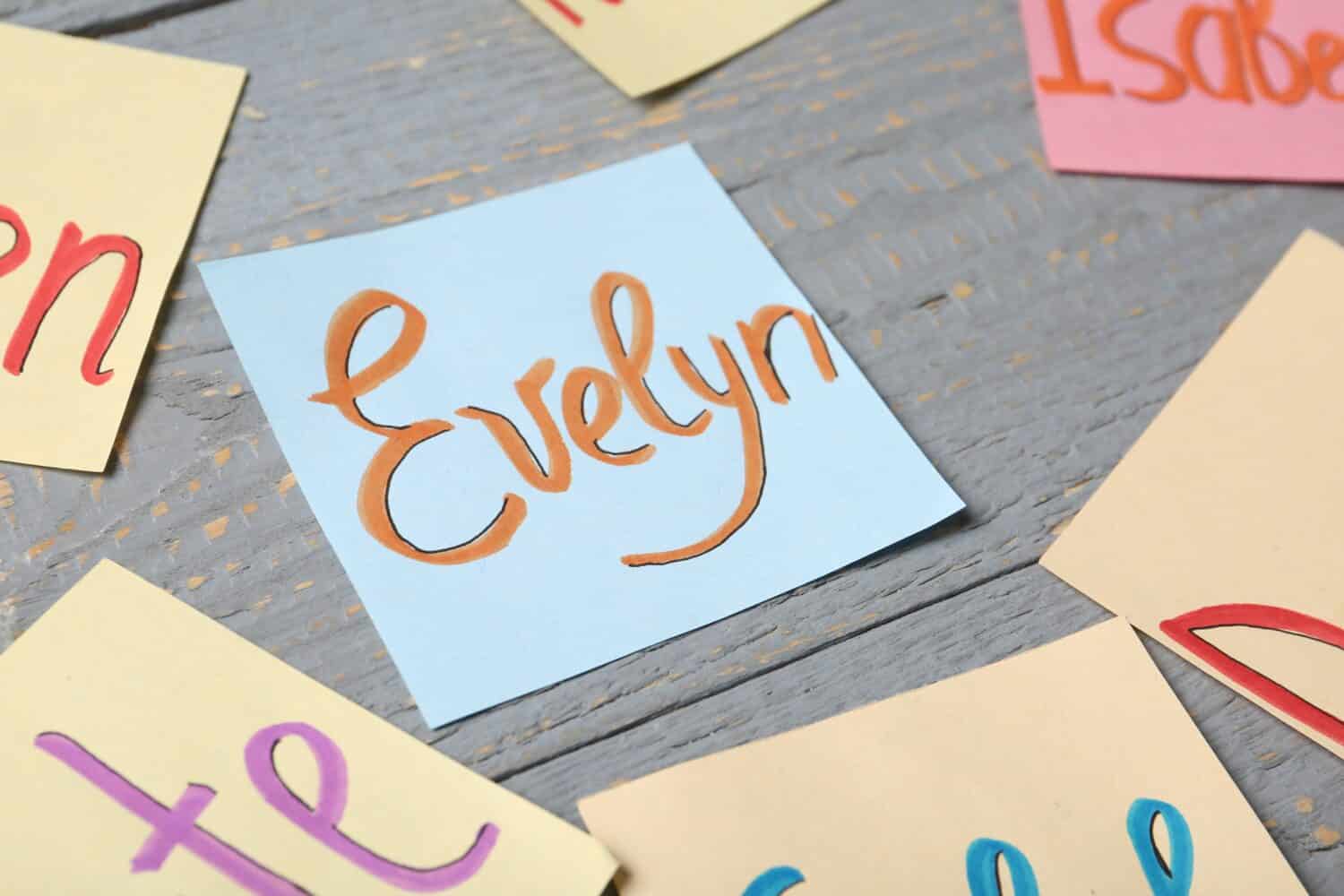 Paper sheet with written baby name Evelyn on grey wooden table, closeup