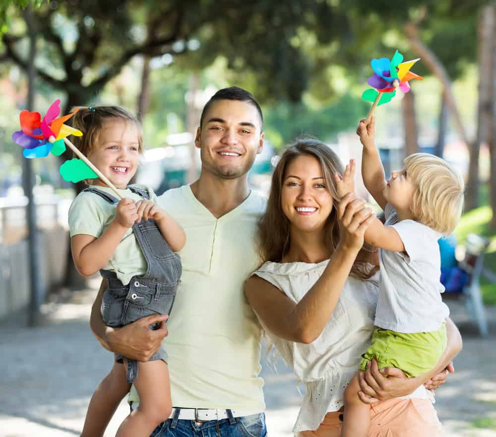 Young parents with children playing windmills in park on vacation day
