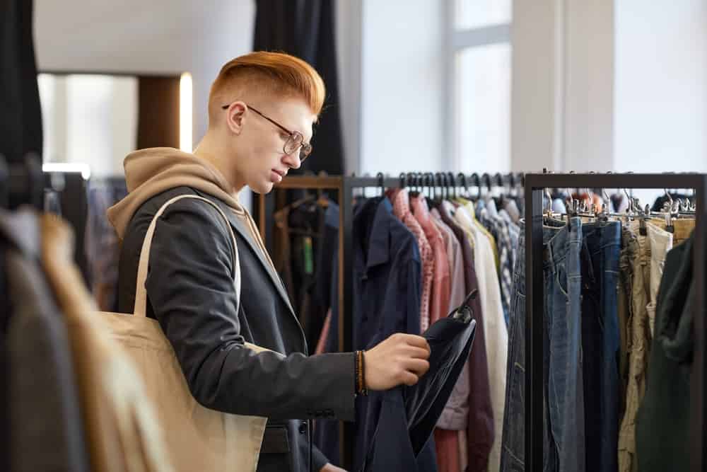 Side view portrait of young man looking at clothes while shopping sustainably in thrift store