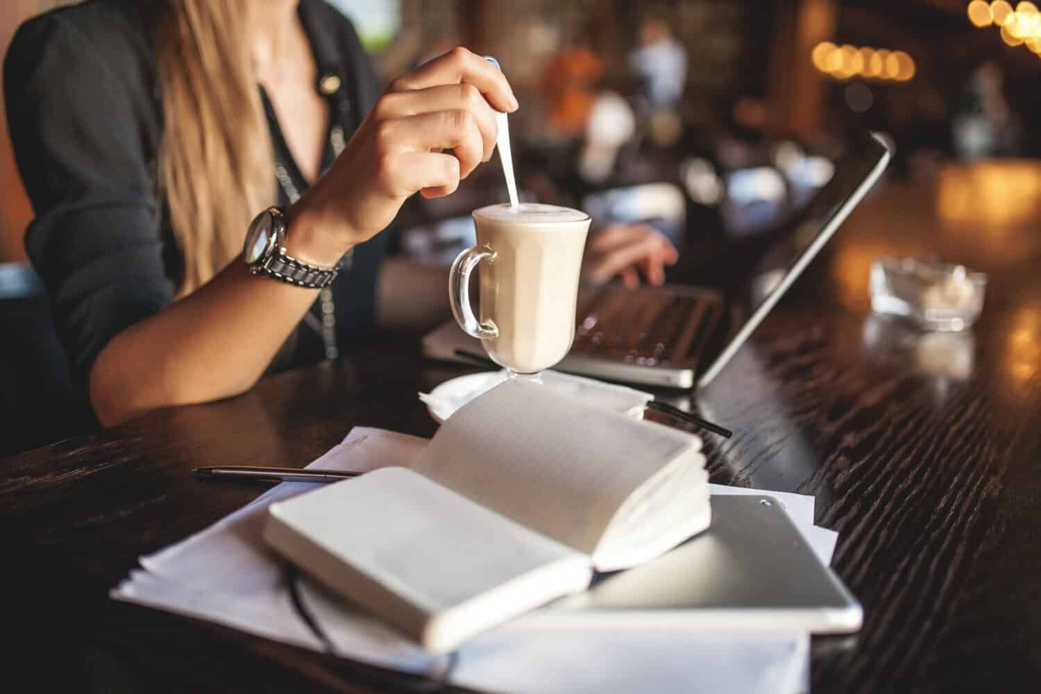 Business woman indoor with coffee and laptop taking notes