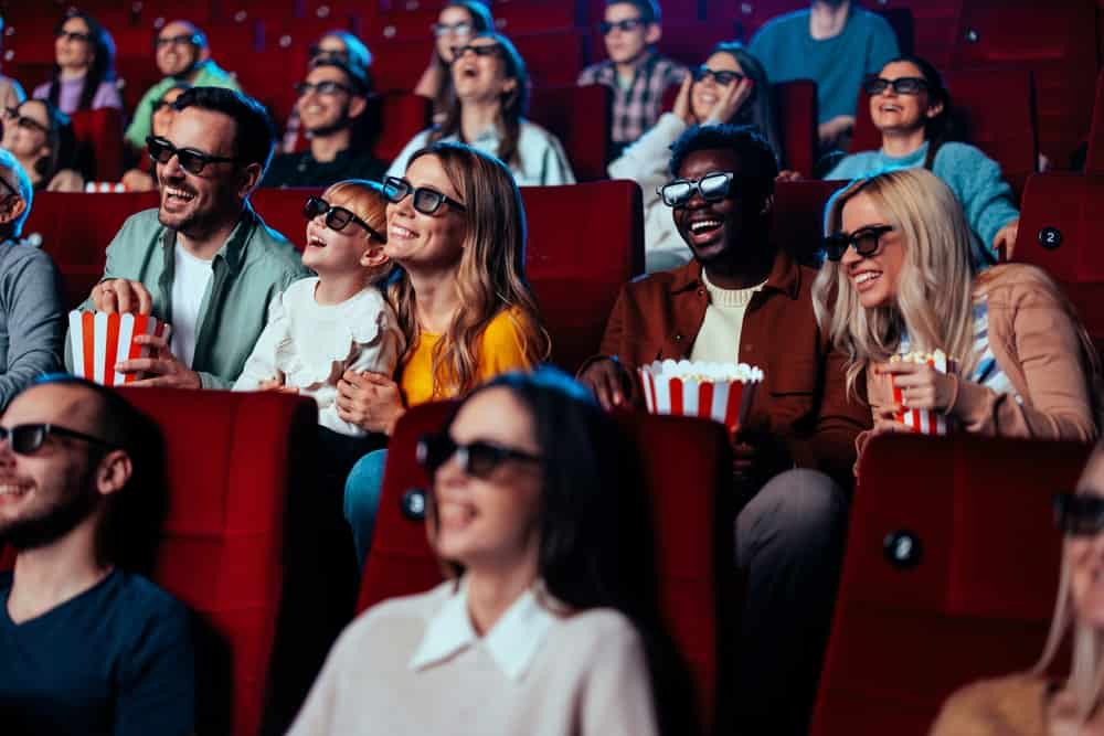 An excited diverse crow is in the movie theater enjoying a 3D movie on the big screen.