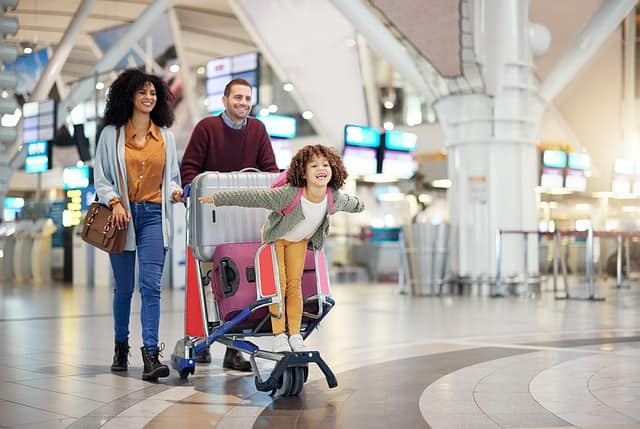Airport, family and child excited for flight with suitcase trolley on holiday, vacation or immigration journey and travel. Luggage of mother, father or diversity parents with girl kid flying in lobby
