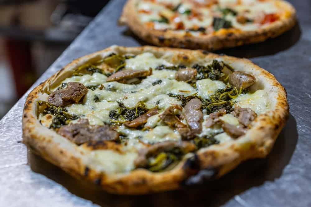 Traditional Neapolitan cartwheel pizza topped with sausage, friarielli and buffalo mozzarella baked in the oven and ready to be served