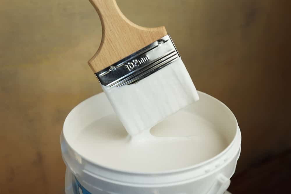 A bucket of white paint and a brush. Painting works in the premises. Tidying up the apartment. Repair of premises. The brush is dipped in white paint